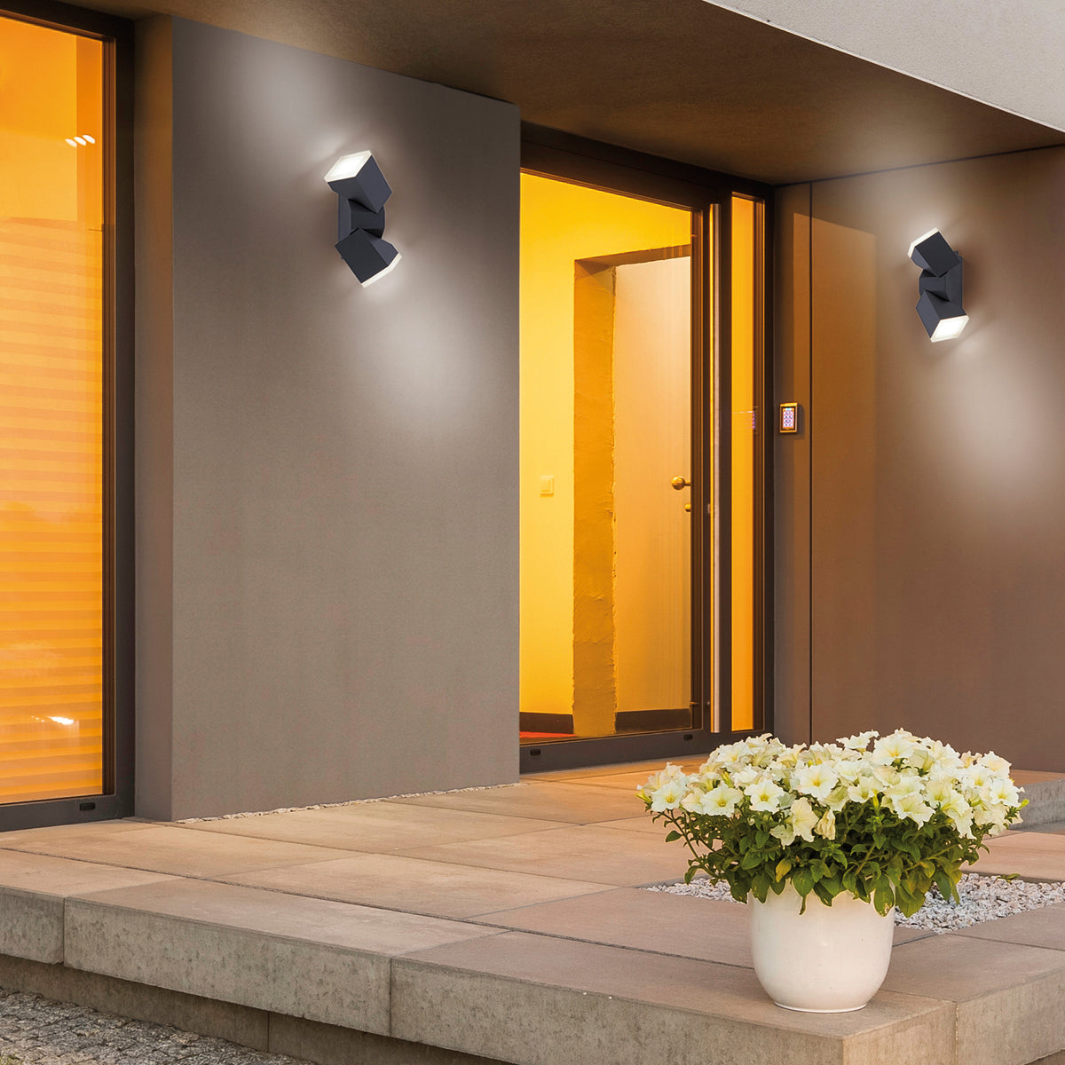 Mise en ambiance extérieure avec deux appliques anthracite éclairant une façade et une entrée.