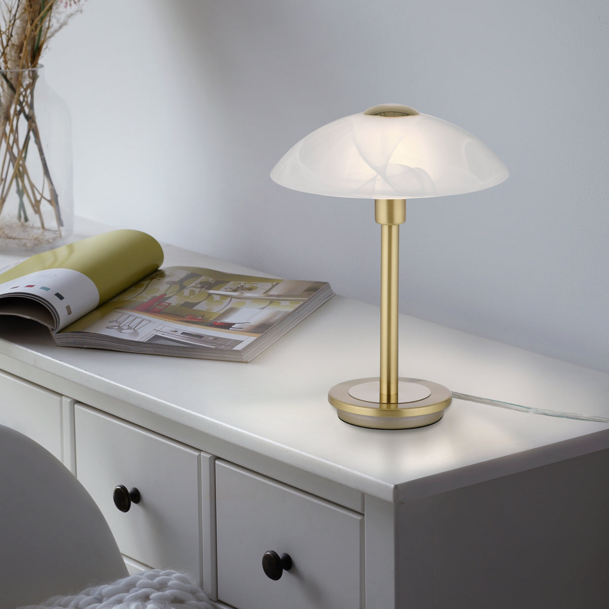 Mise en ambiance sur une commode blanche avec magazines, lumière chaude allumée
