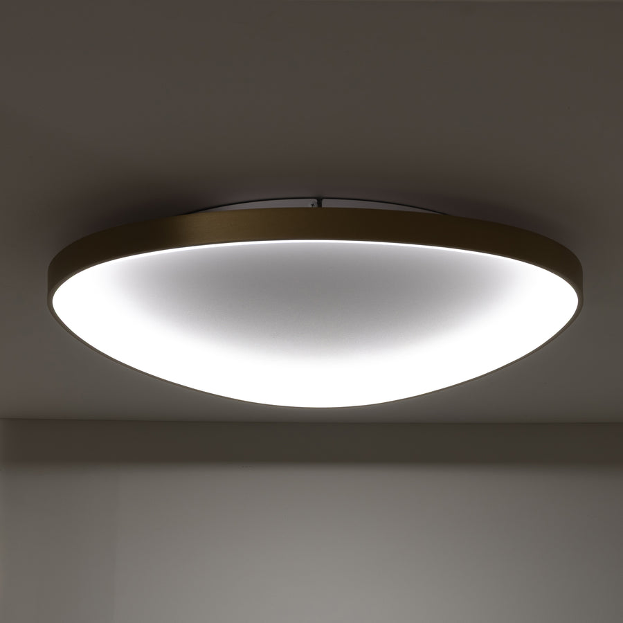 Plafonnier allumé de face, cadre doré et large diffuseur blanc dans une pièce sombre.