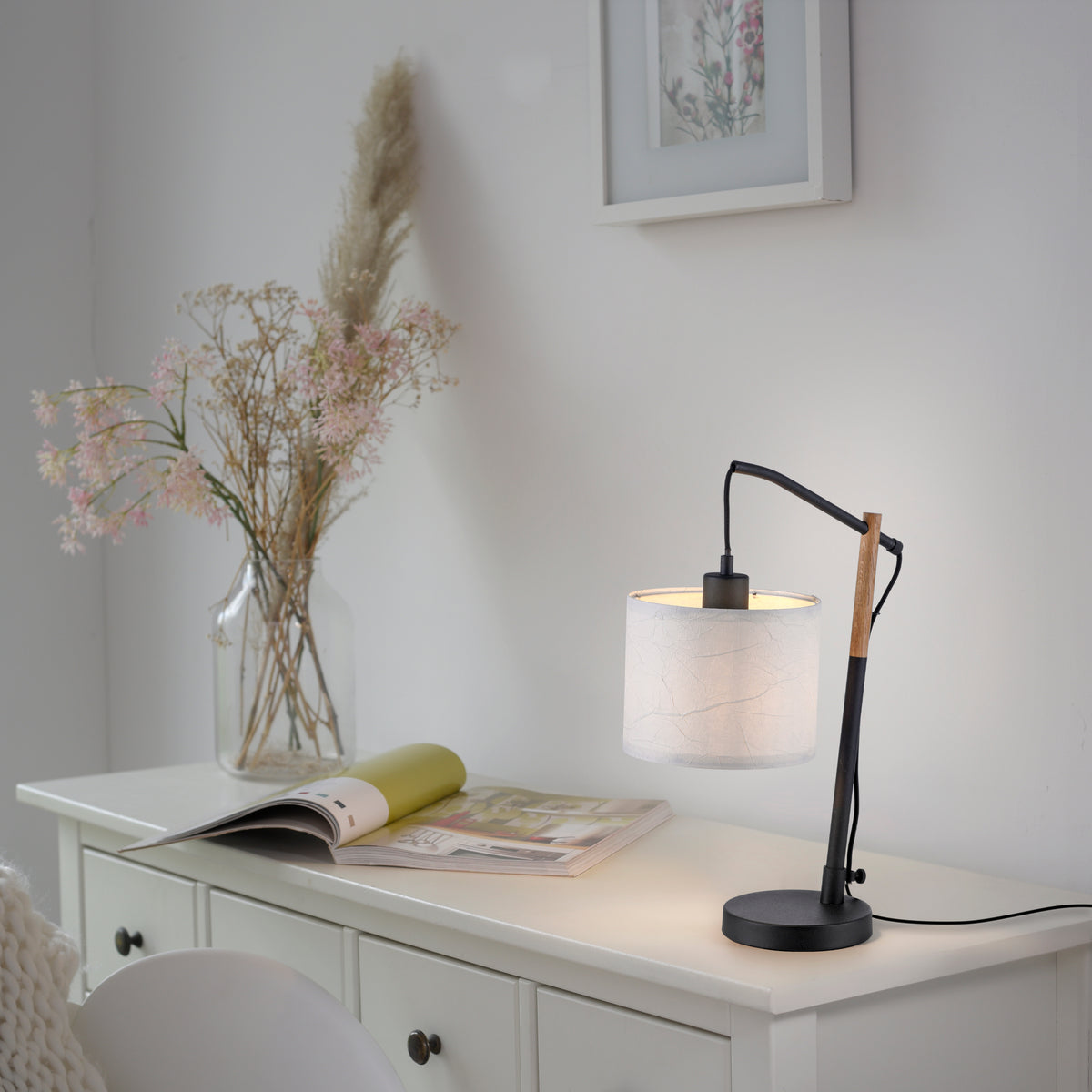 Mise en ambiance sur commode blanche, lampe allumée près d'un vase et magazine