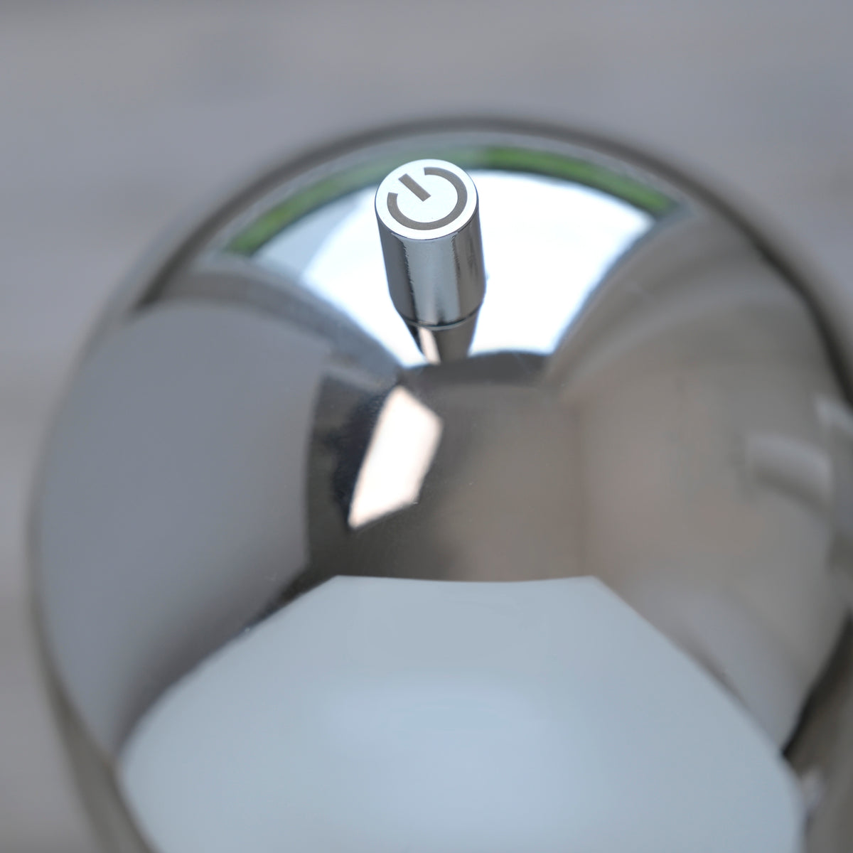 Gros plan sur le bouton tactile avec symbole marche-arrêt au sommet du luminaire chromé.