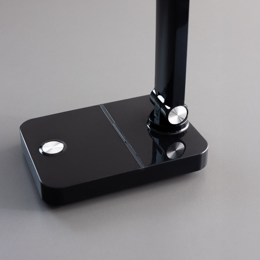 Gros plan sur la base noire brillante, bouton tactile et articulation chromée de la lampe.