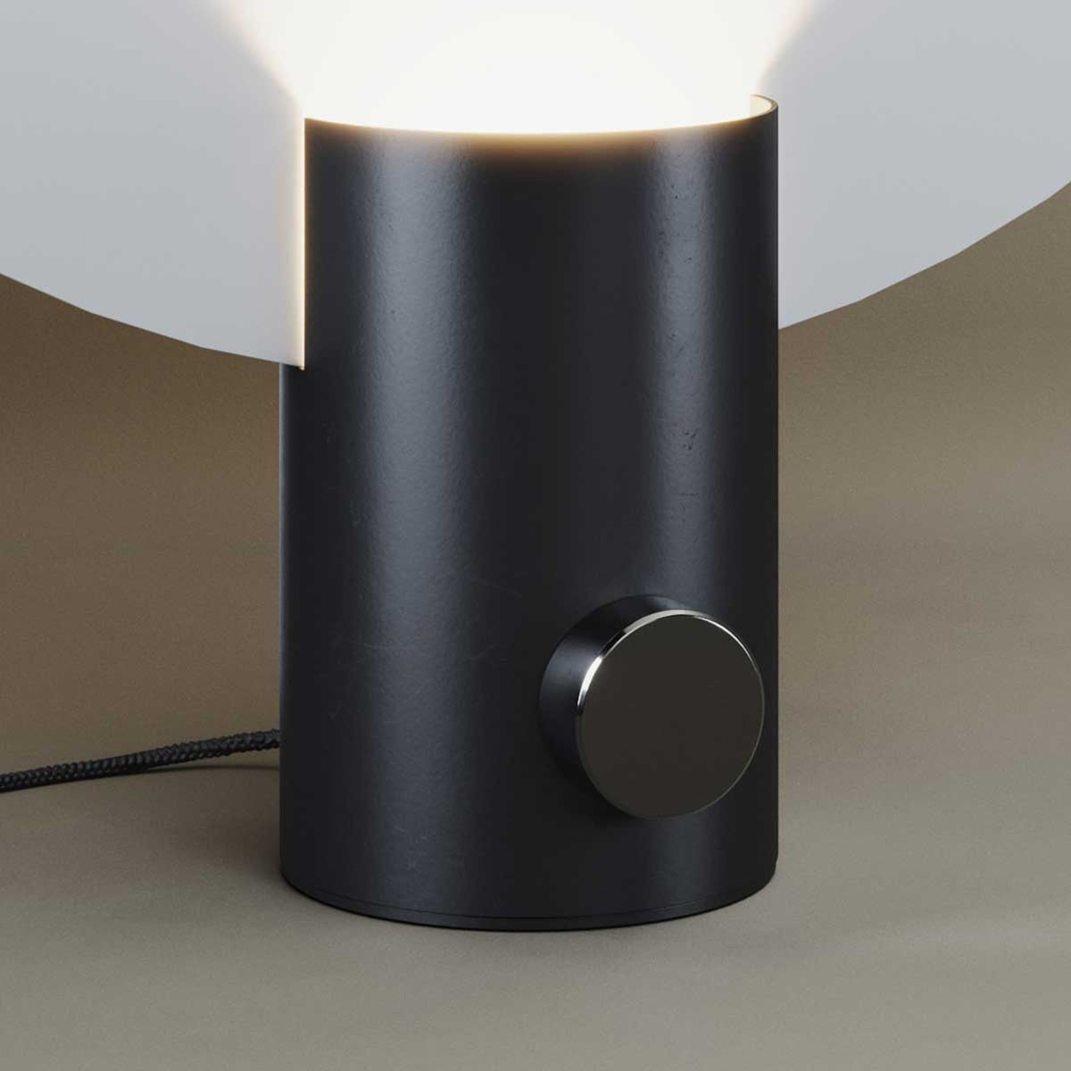 Détail du socle cylindrique noir mat avec bouton variateur et cordon tressé.