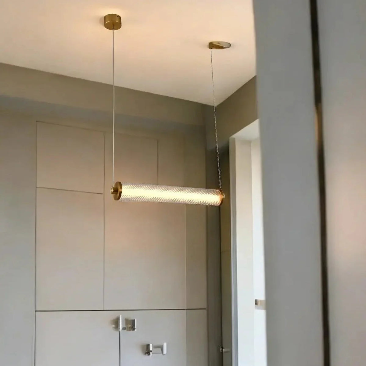 Suspension cylindrique horizontale allumée, installée devant des placards muraux clairs