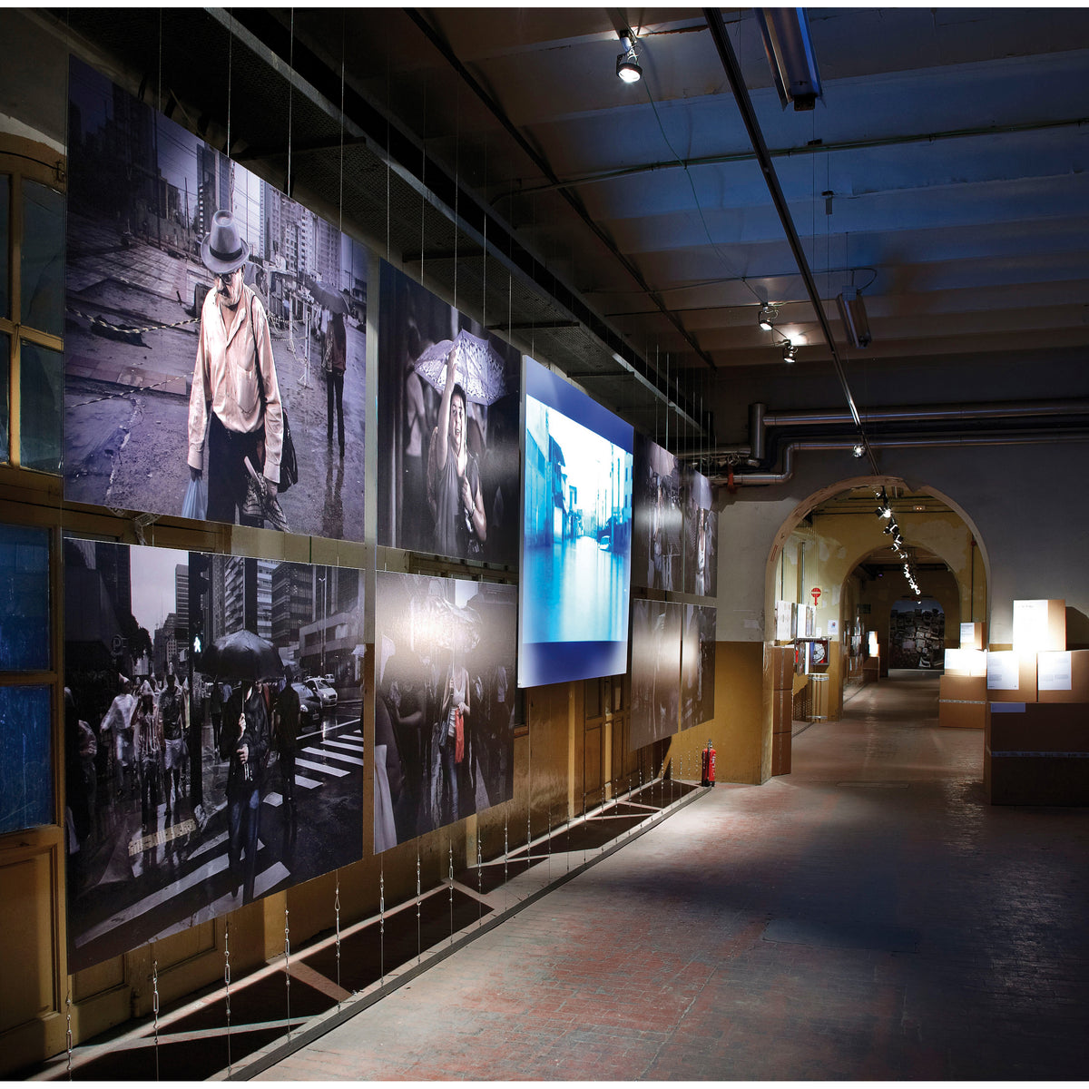 Spot sur rail éclairant des photographies suspendues dans une galerie sombre.