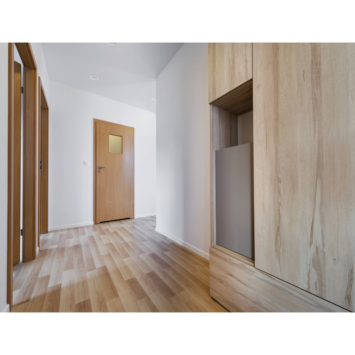 Couloir avec parquet clair, portes en bois et spots encastrés au plafond.