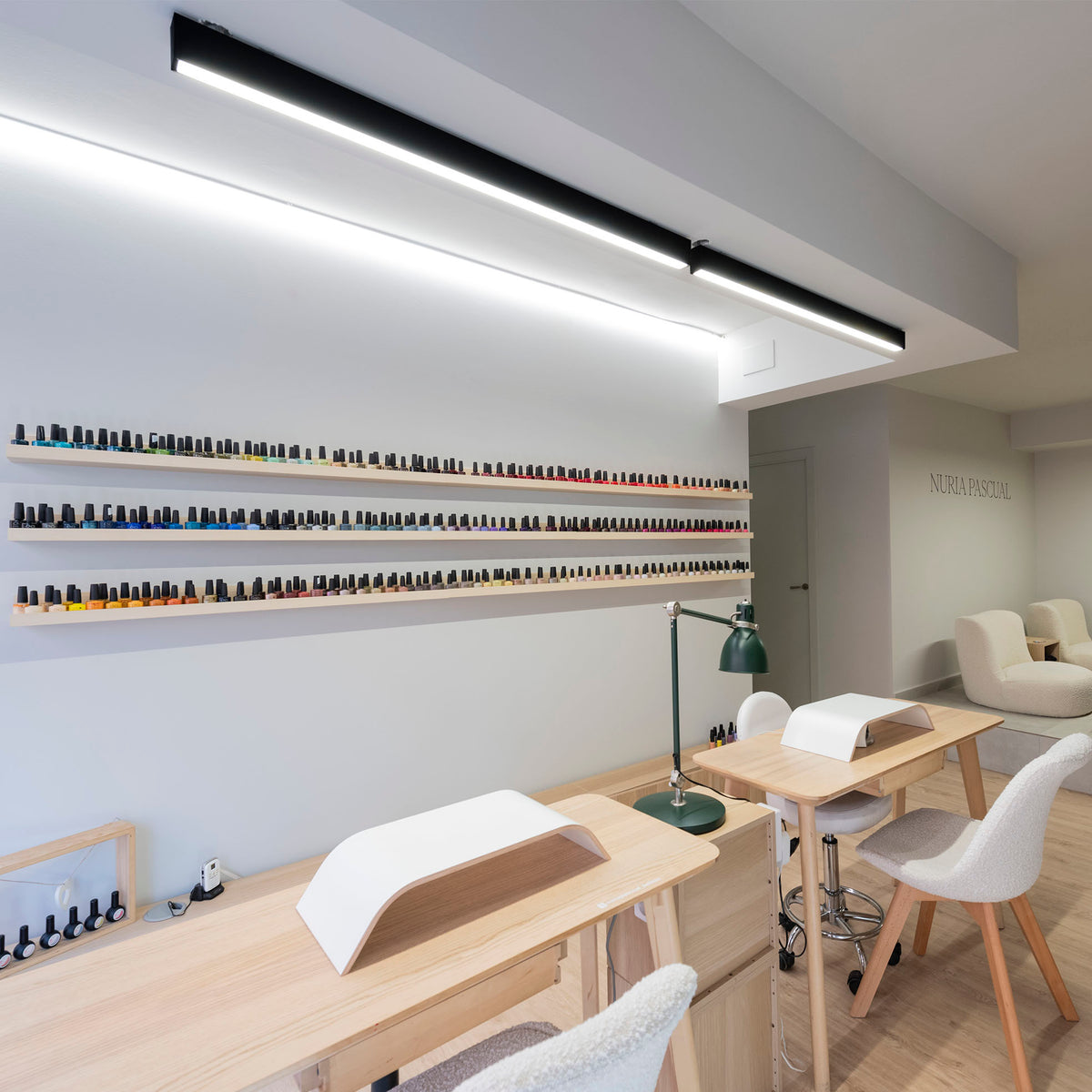 Deux plafonniers linéaires noirs éclairent un salon de manucure et ses étagères.