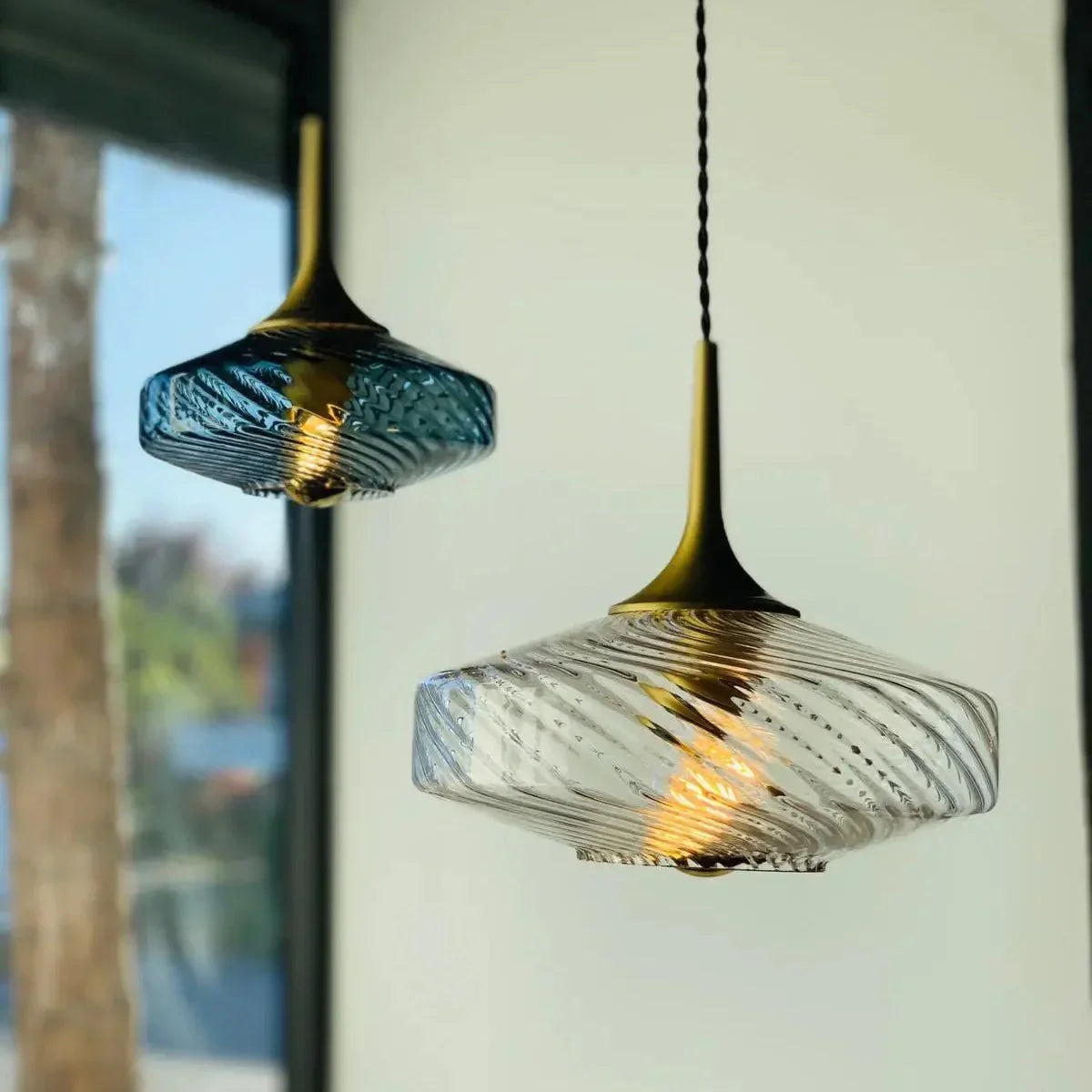 Gros plan sur deux luminaires, verre bleu et transparent à motifs torsadés.
