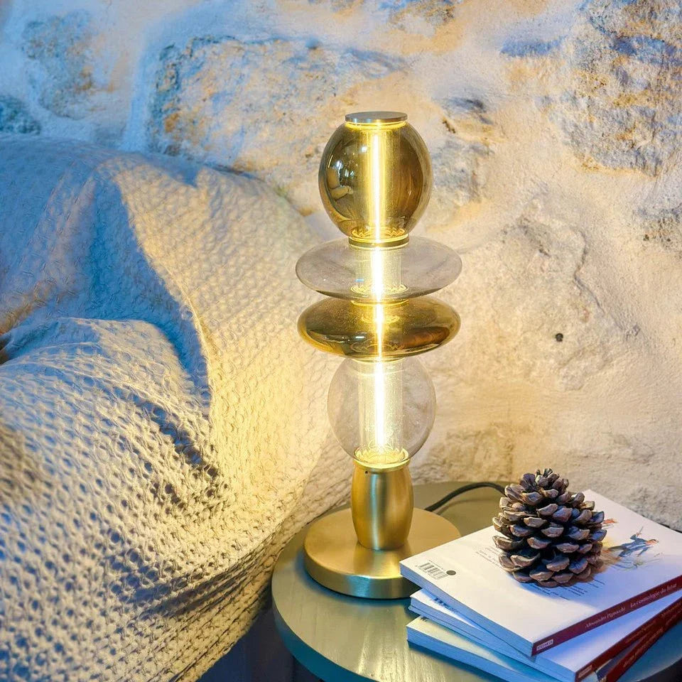 Lampe de table dorée allumée près d'un livre et d'une pomme de pin, intérieur pierre.