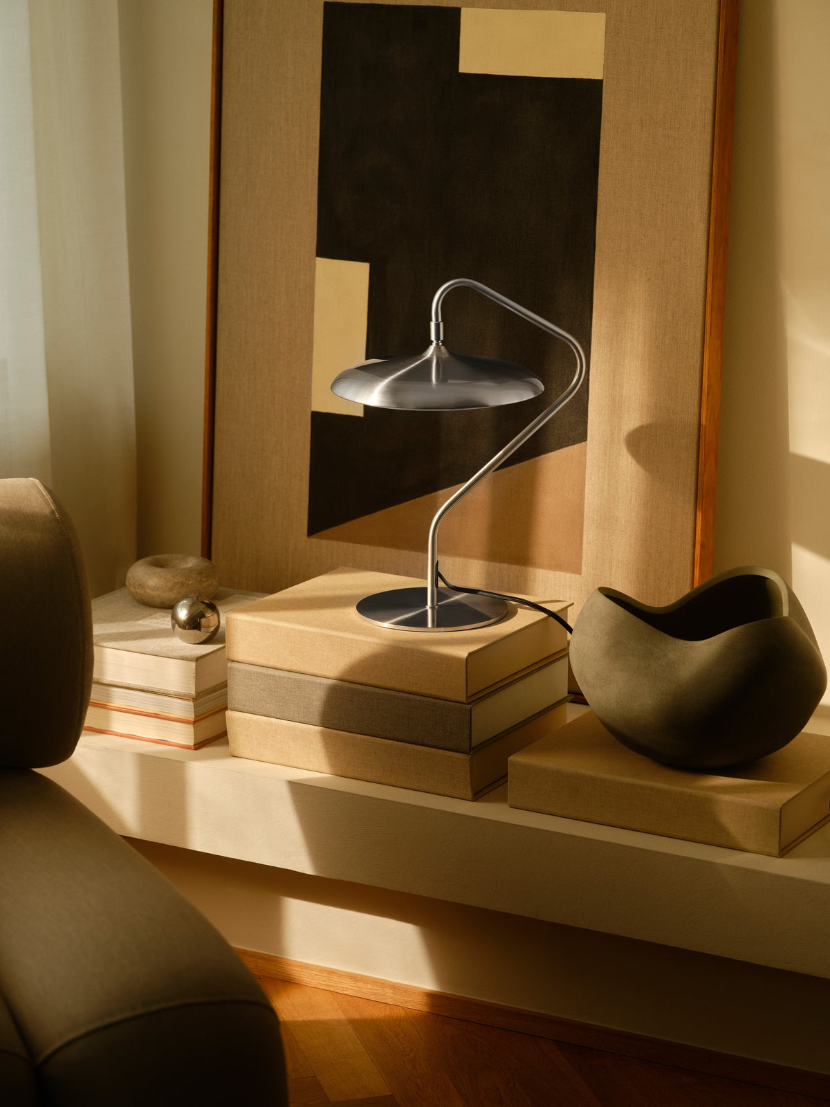 Mise en ambiance chaleureuse avec lampe posée sur des livres, toile abstraite et vase foncé.