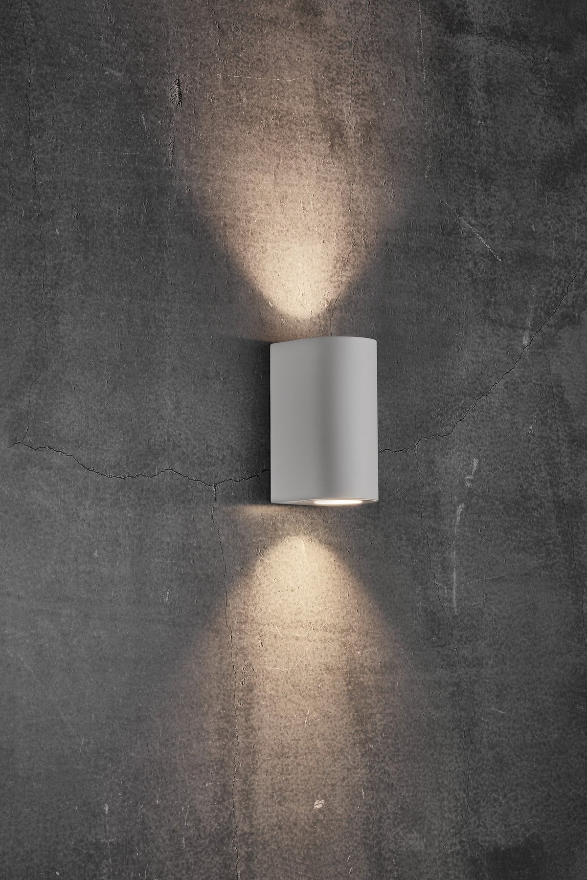 Mise en ambiance : applique blanche installée sur un mur béton, éclairage haut et bas.
