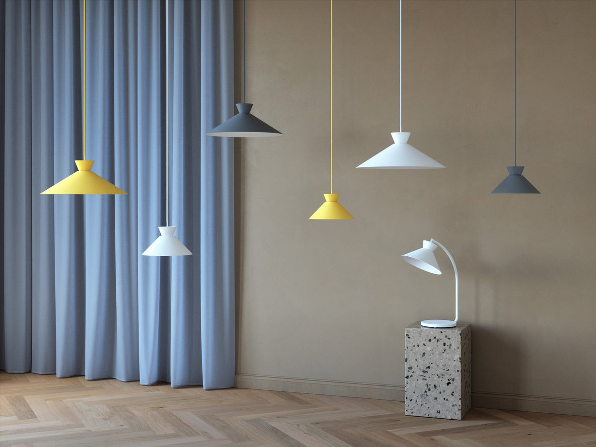 Plusieurs suspensions colorées jaune, gris et blanc, une lampe de table blanche sur cube.
