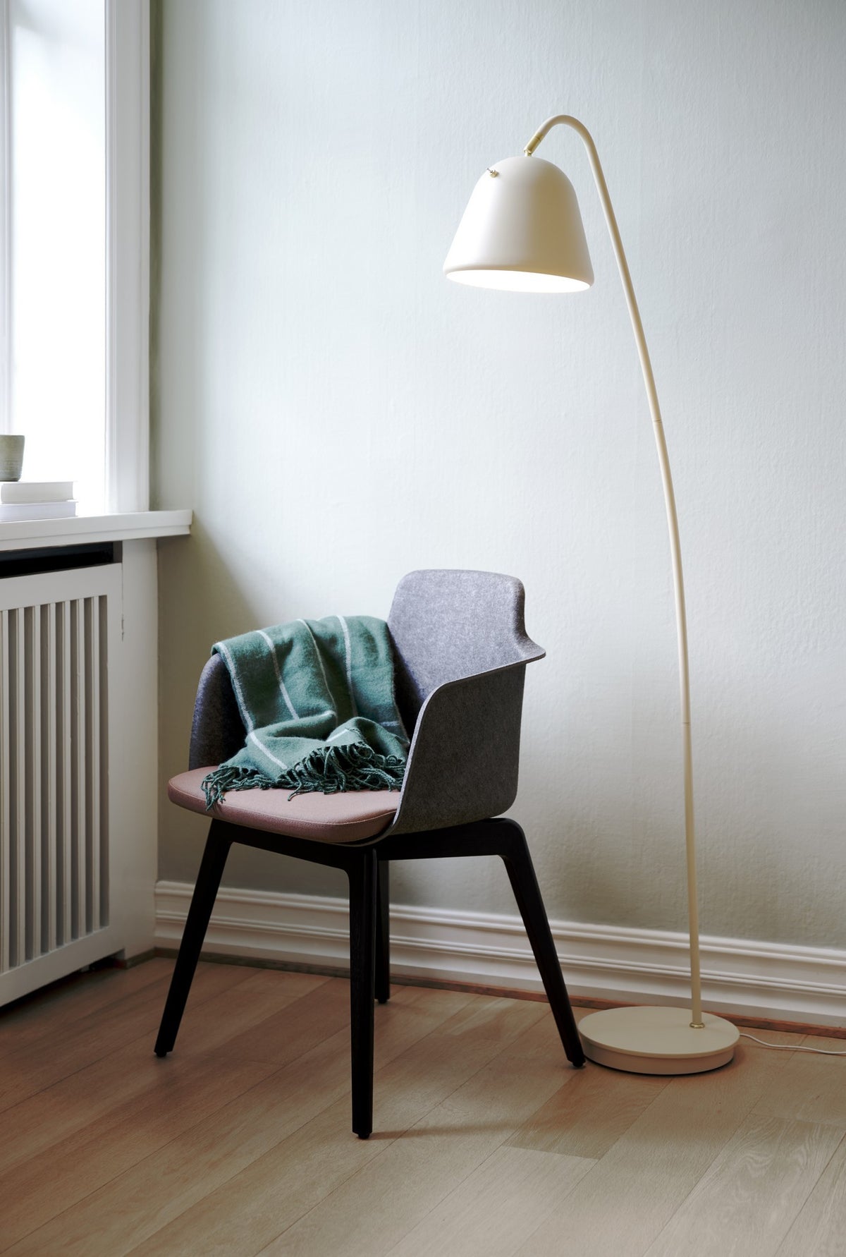 Mise en ambiance : lampadaire beige éclairant un fauteuil gris couvert d'un plaid vert.