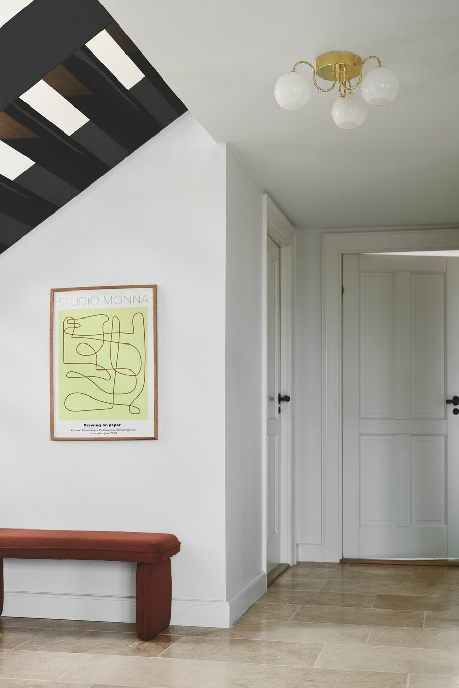 Plafonnier doré à trois globes installé au plafond d'un couloir blanc lumineux.