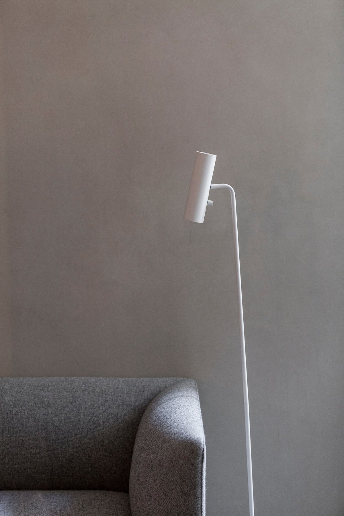 Détail du luminaire blanc placé près d'un fauteuil gris, fond mural uni
