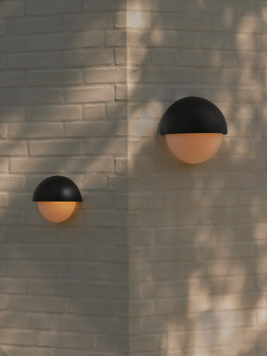 Vue sur mur de briques avec deux appliques noires installées et ombres
