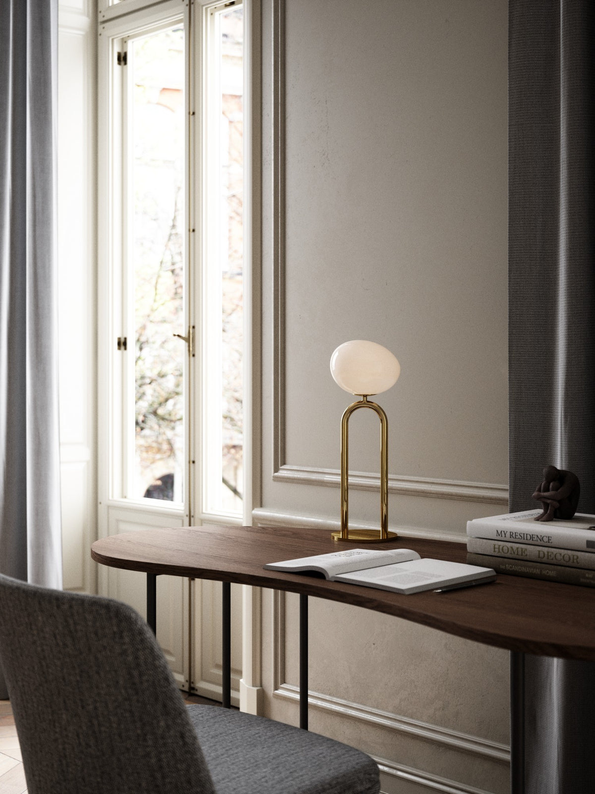 Lampe à poser en laiton sur un bureau en bois, livre ouvert près d'une fenêtre.