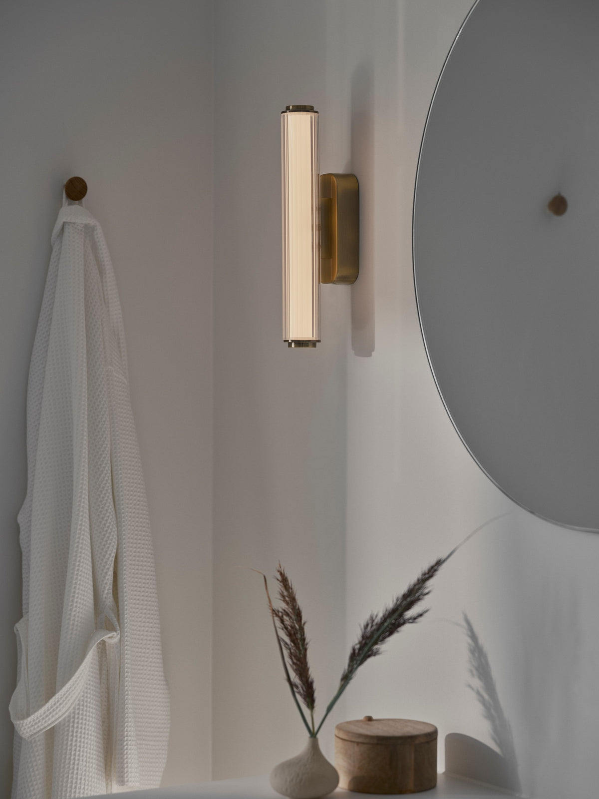 Applique allumée au-dessus d’un lavabo, près d’un miroir rond et d’une serviette blanche.
