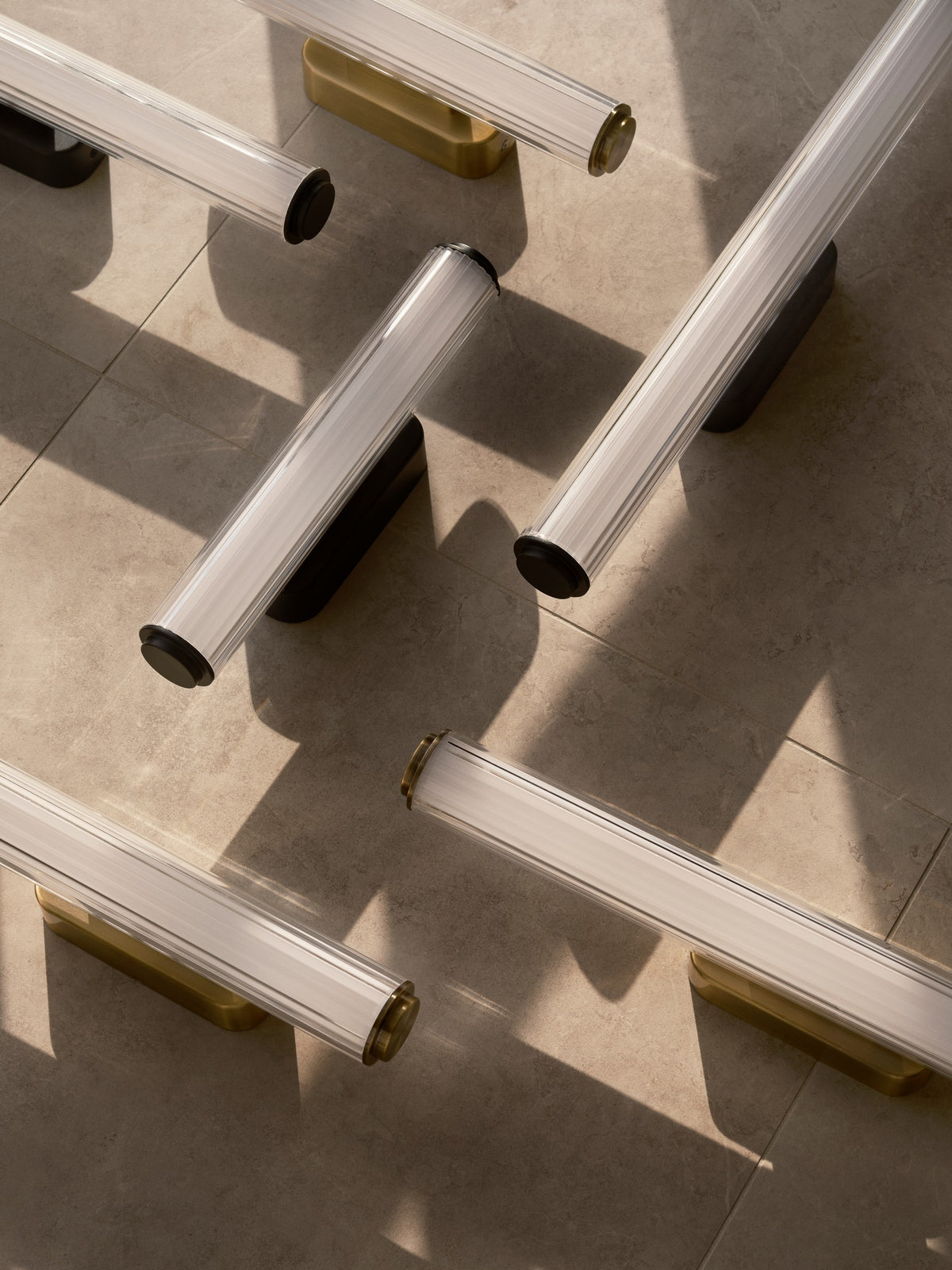 Plusieurs appliques dorées et noires posées au sol, ombres marquées sur carrelage beige.