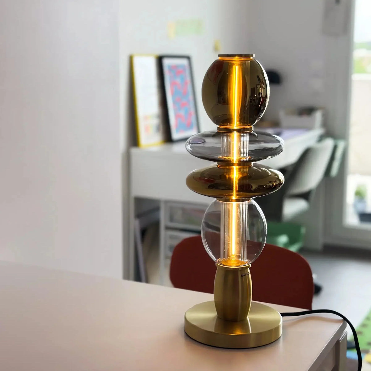 Lampe de table dorée et verre fumé, gros plan de face sur une table blanche.