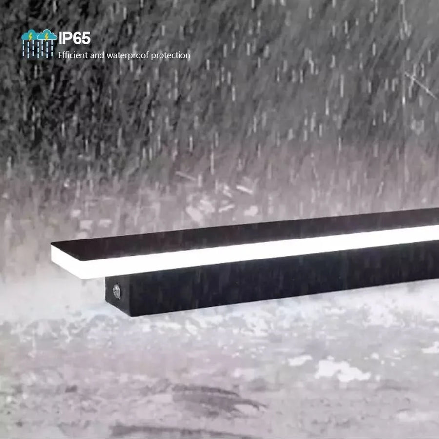 Détail produit sous une pluie battante, applique linéaire noire avec mention IP65 étanche.