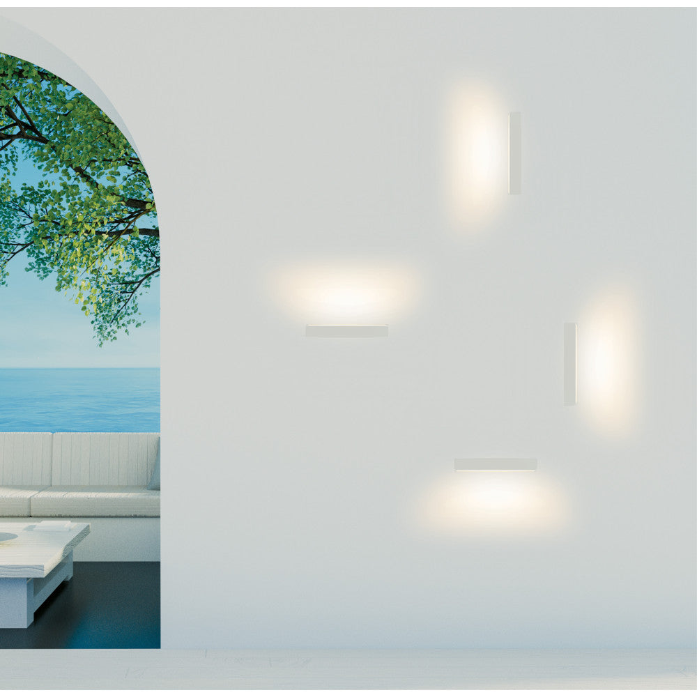 Mise en ambiance extérieure : quatre appliques allumées sur mur blanc, vue mer et feuillage.
