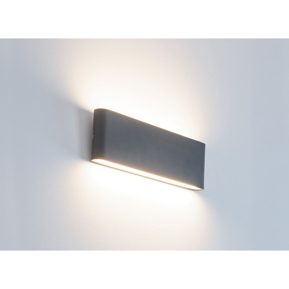 Luminaire mural éclairé, fixé sur un mur blanc, halo lumineux vers le bas.