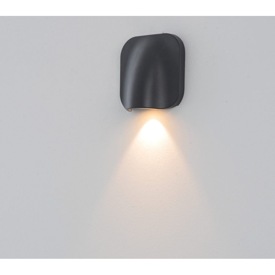 Applique graphite installée sur un mur clair, éclairant vers le bas d'un halo chaud