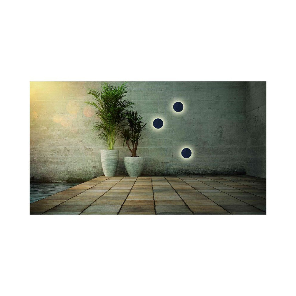 Mise en ambiance extérieure avec trois appliques rondes éclairées sur mur béton et plantes.