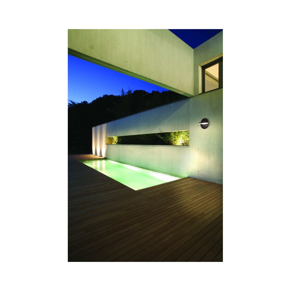 Vue nocturne de l'applique ronde éclairant une terrasse en bois devant une piscine.