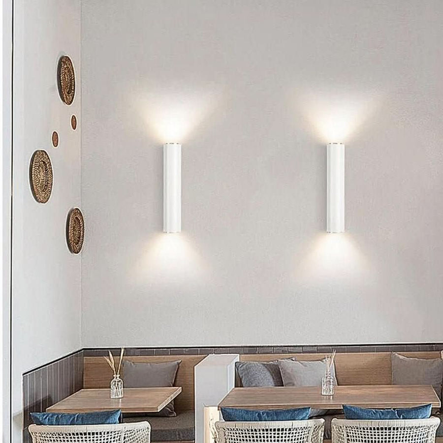 Deux appliques murales blanches éclairant un mur blanc au-dessus d'une banquette de restaurant.