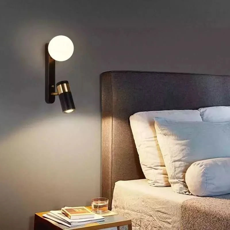 Applique murale noire et dorée installée près d'un lit aux coussins clairs