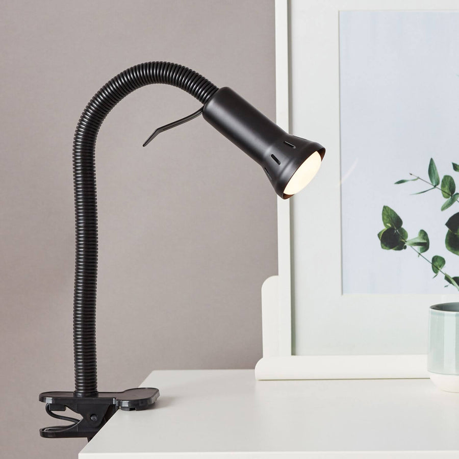 Lampe de bureau noire fixée par pince sur bureau blanc, cadre et eucalyptus.