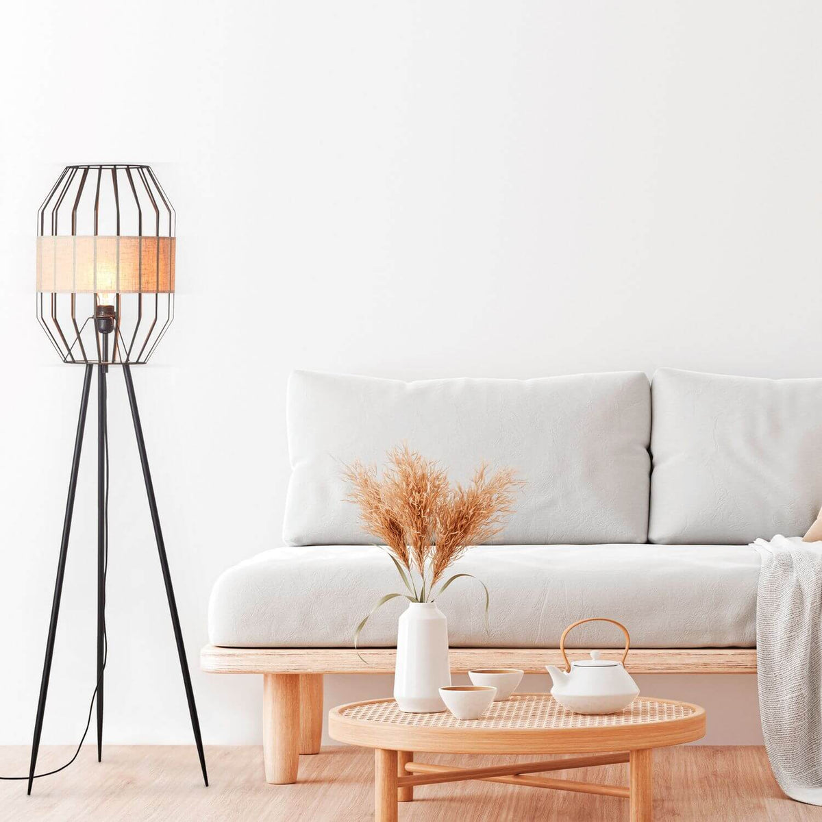 Lampadaire allumé près d'un canapé blanc, table basse rotin et pampas