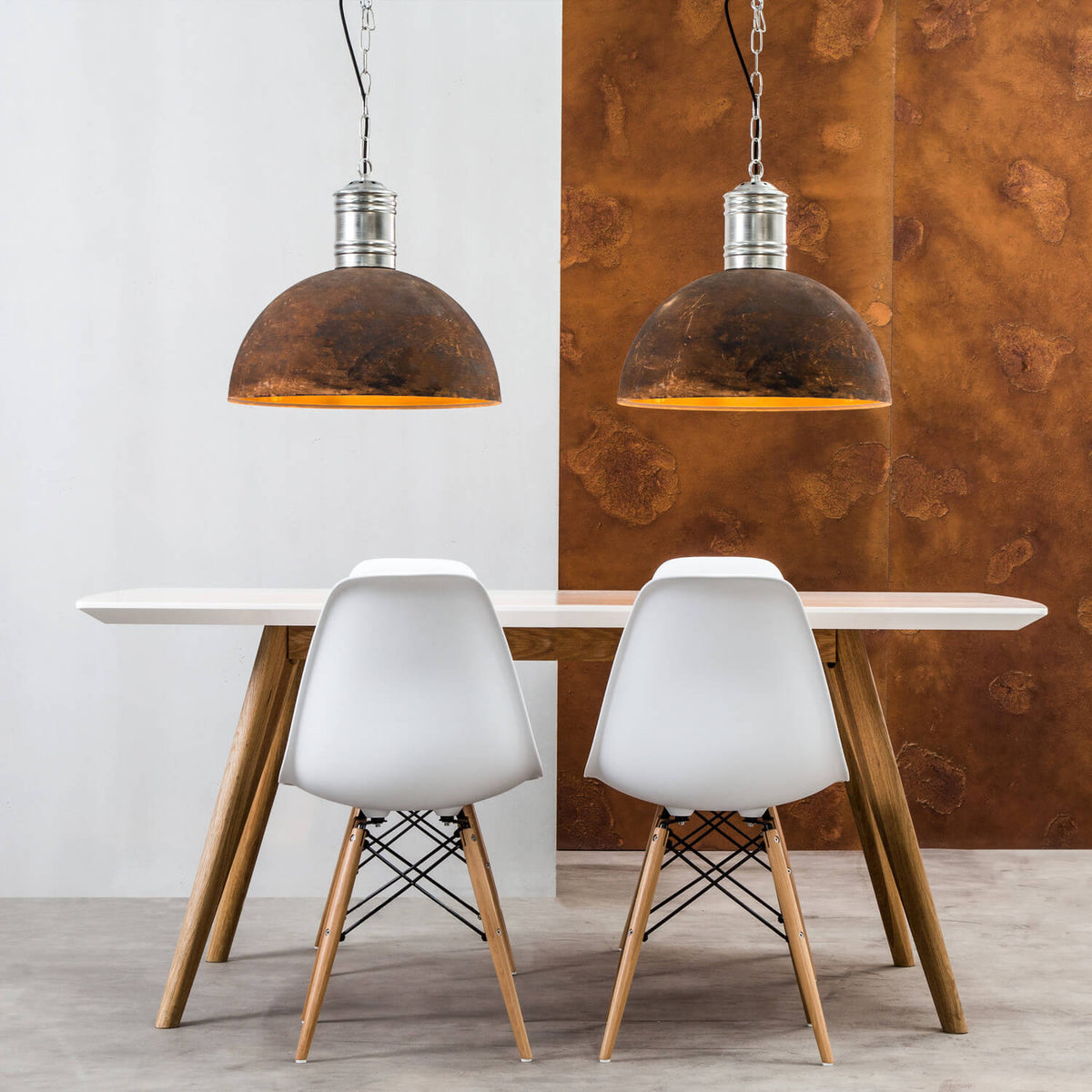 Deux suspensions identiques au-dessus d'une table blanche, décor mural rouille et chaises.