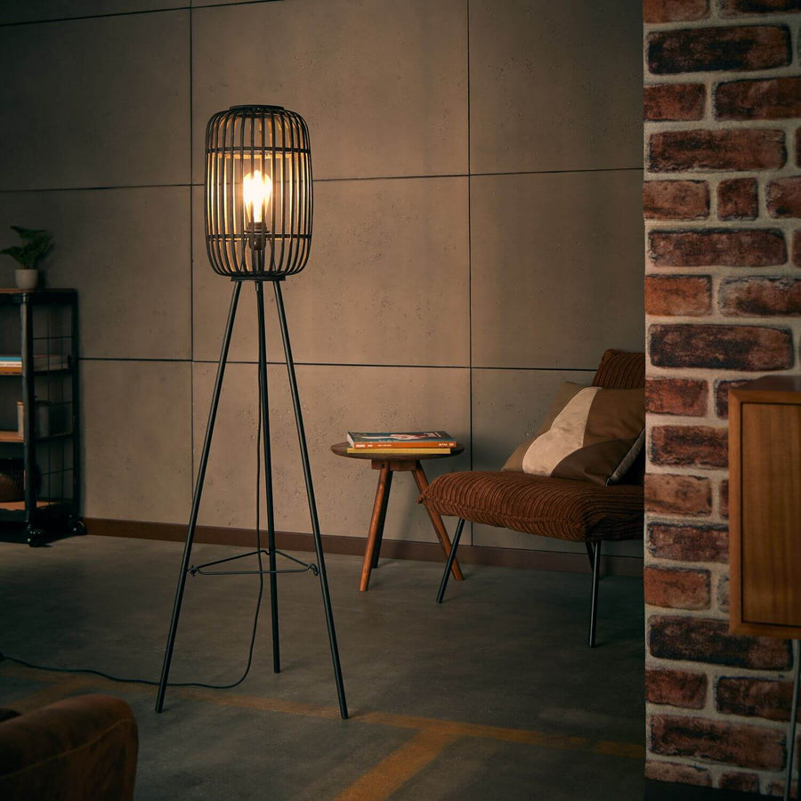 Lampadaire allumé dans un salon, près d'un fauteuil et d'une table basse, mur en briques.