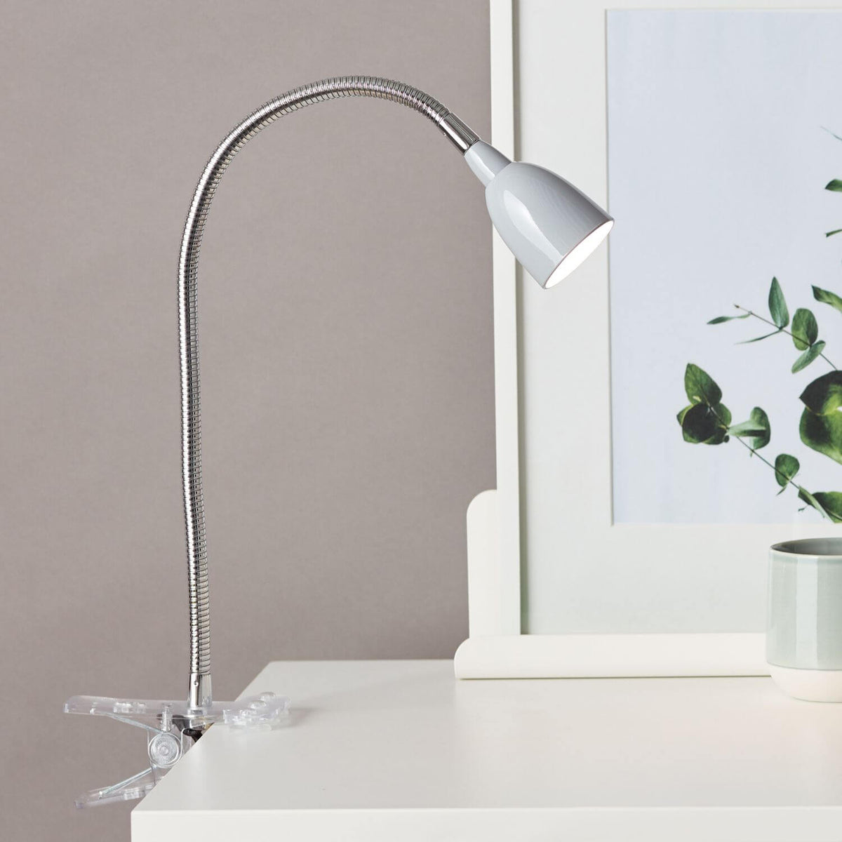 Lampe pincée au bord d'une table, tête grise allumée dirigée vers le bas