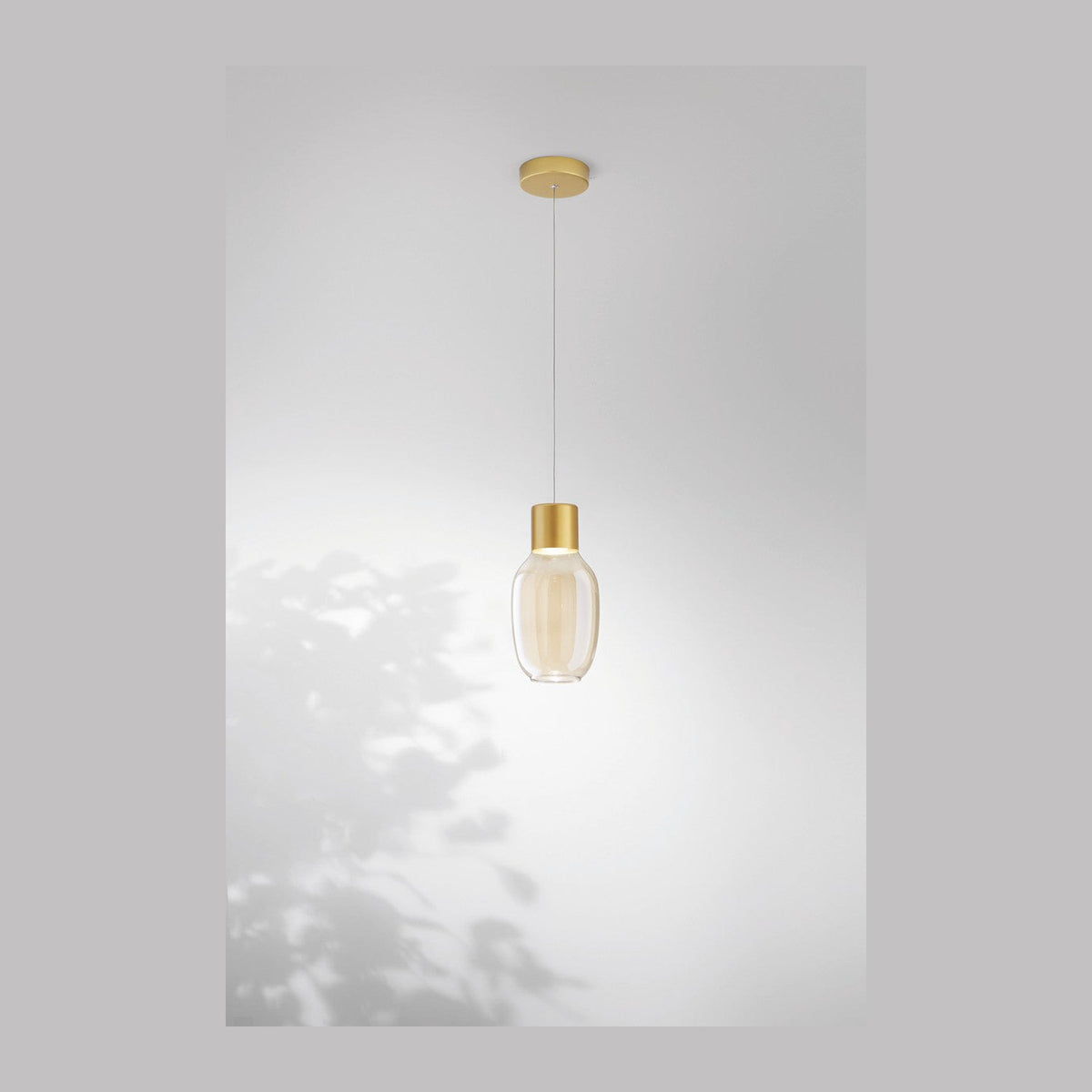 Suspension au verre transparent ovale et douille dorée, vue de face sur fond clair