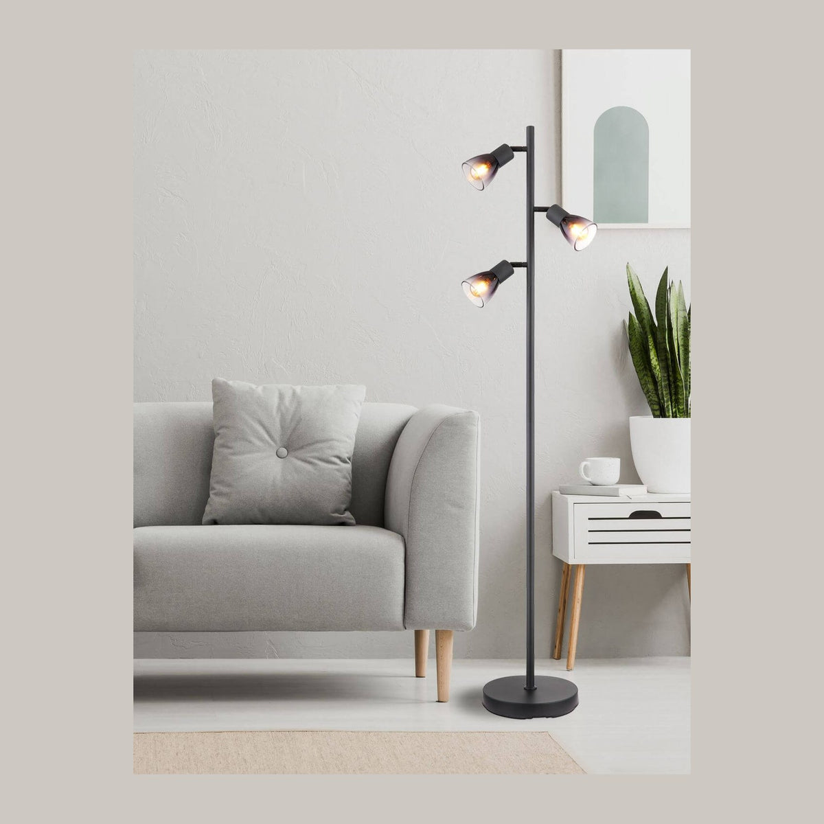 Lampadaire noir allumé dans un salon gris, près d'un canapé, d'un tableau et d'une plante