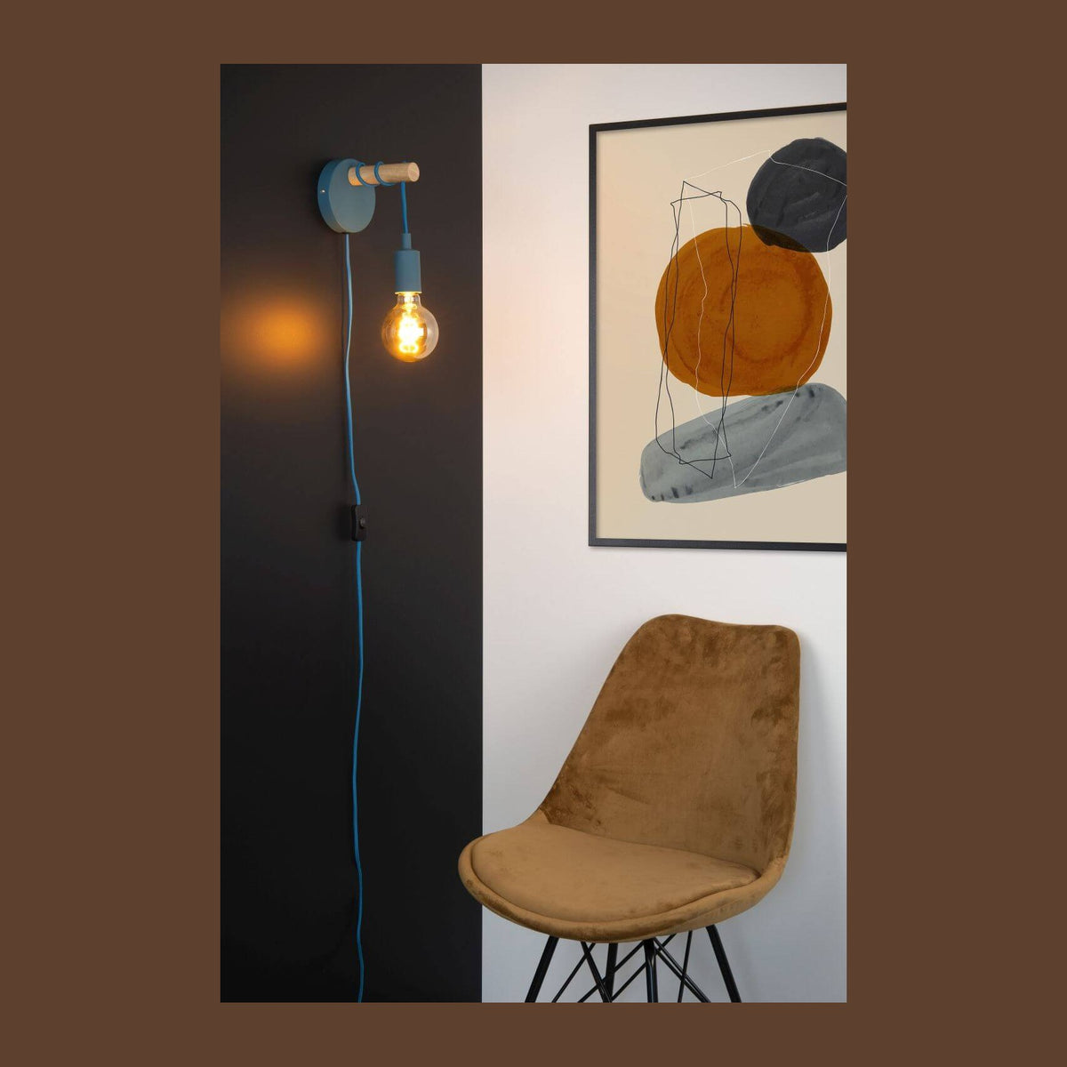 Mise en ambiance de l'applique bleue allumée sur un mur noir, fauteuil et cadre.