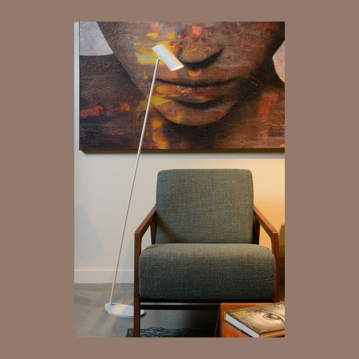 Lampadaire blanc incliné dans un salon devant un fauteuil vert et une toile