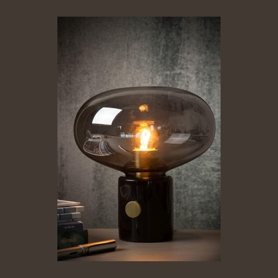 Vue de face du luminaire allumé, socle noir brillant, fond gris texturé.