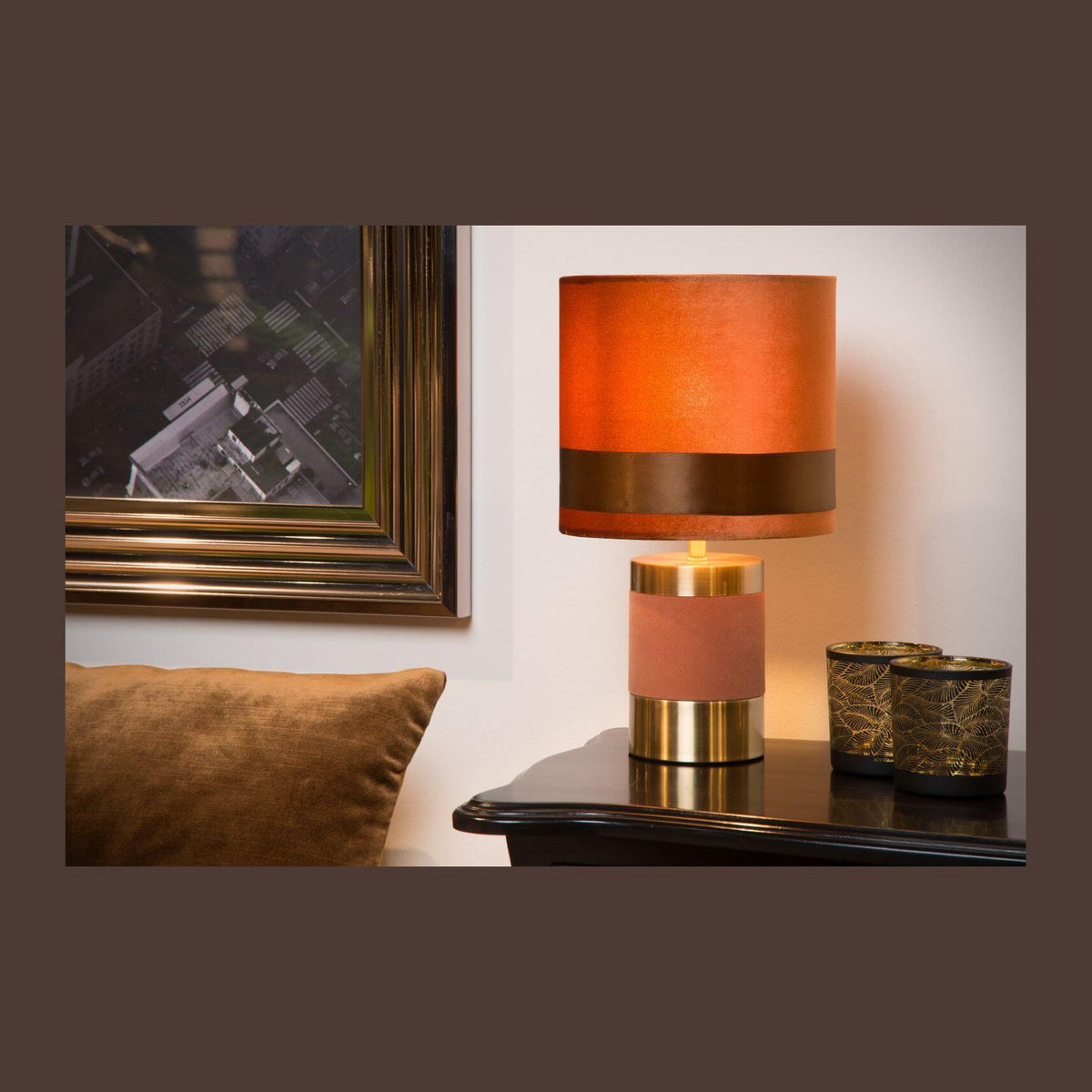 Lampe posée sur une table de nuit noire, cadre doré et coussin marron en arrière-plan