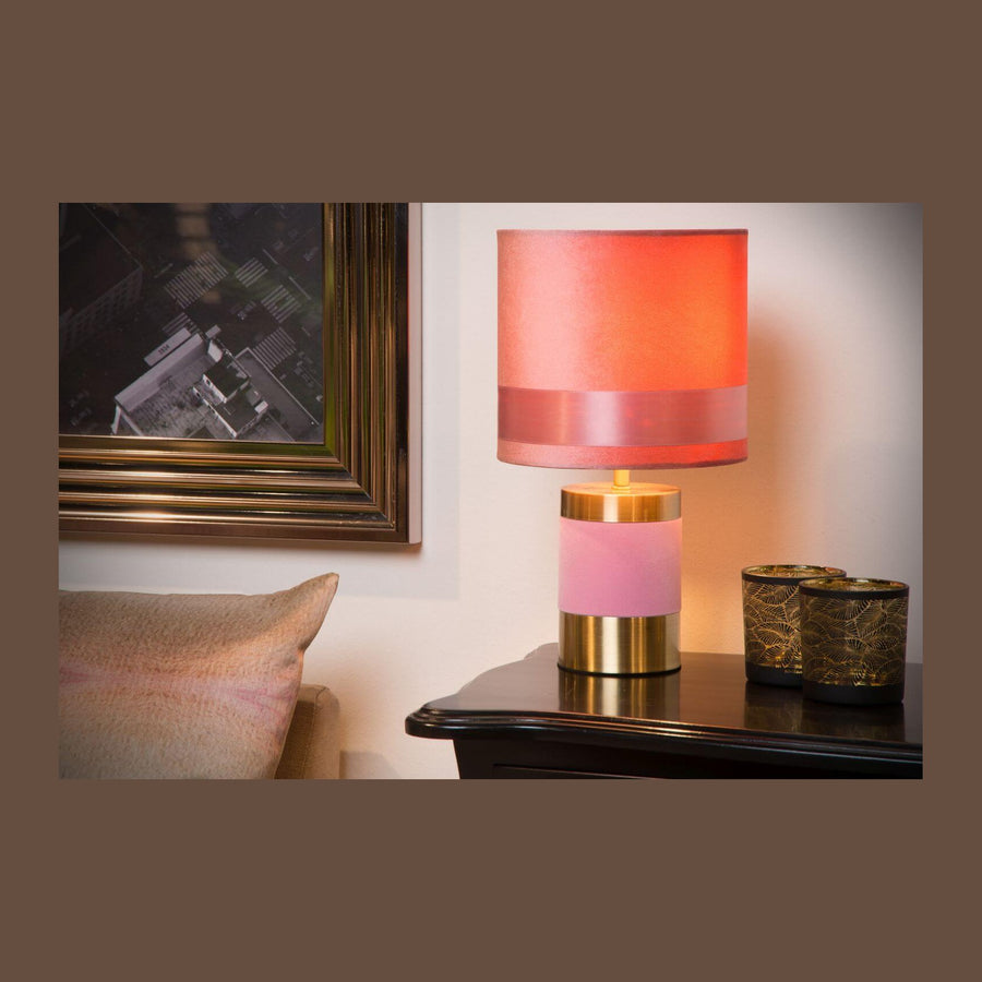 Lampe à poser rose et dorée posée sur une table de chevet avec cadre photo