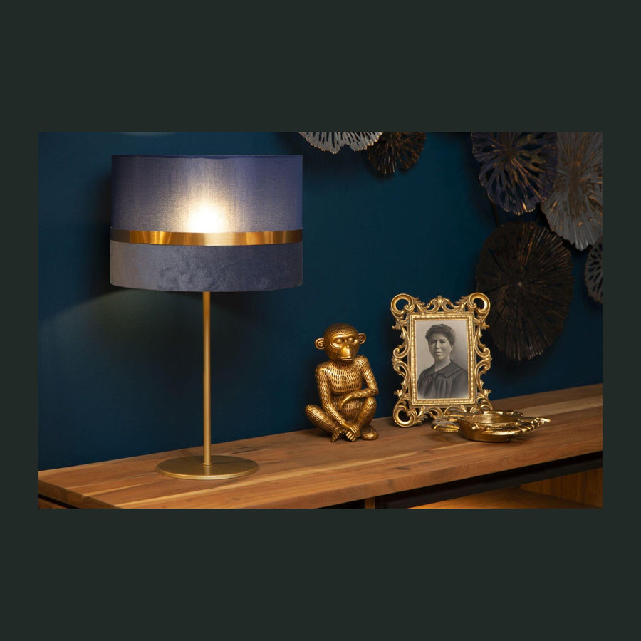 Lampe à poser bleu nuit et dorée allumée sur un meuble en bois.