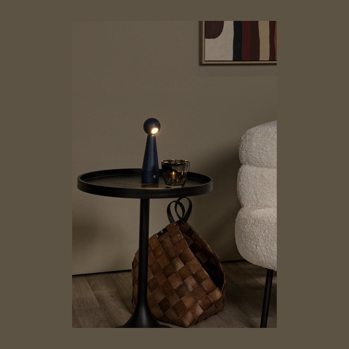 Lampe bleue allumée posée sur une table d'appoint noire avec une tasse en verre.