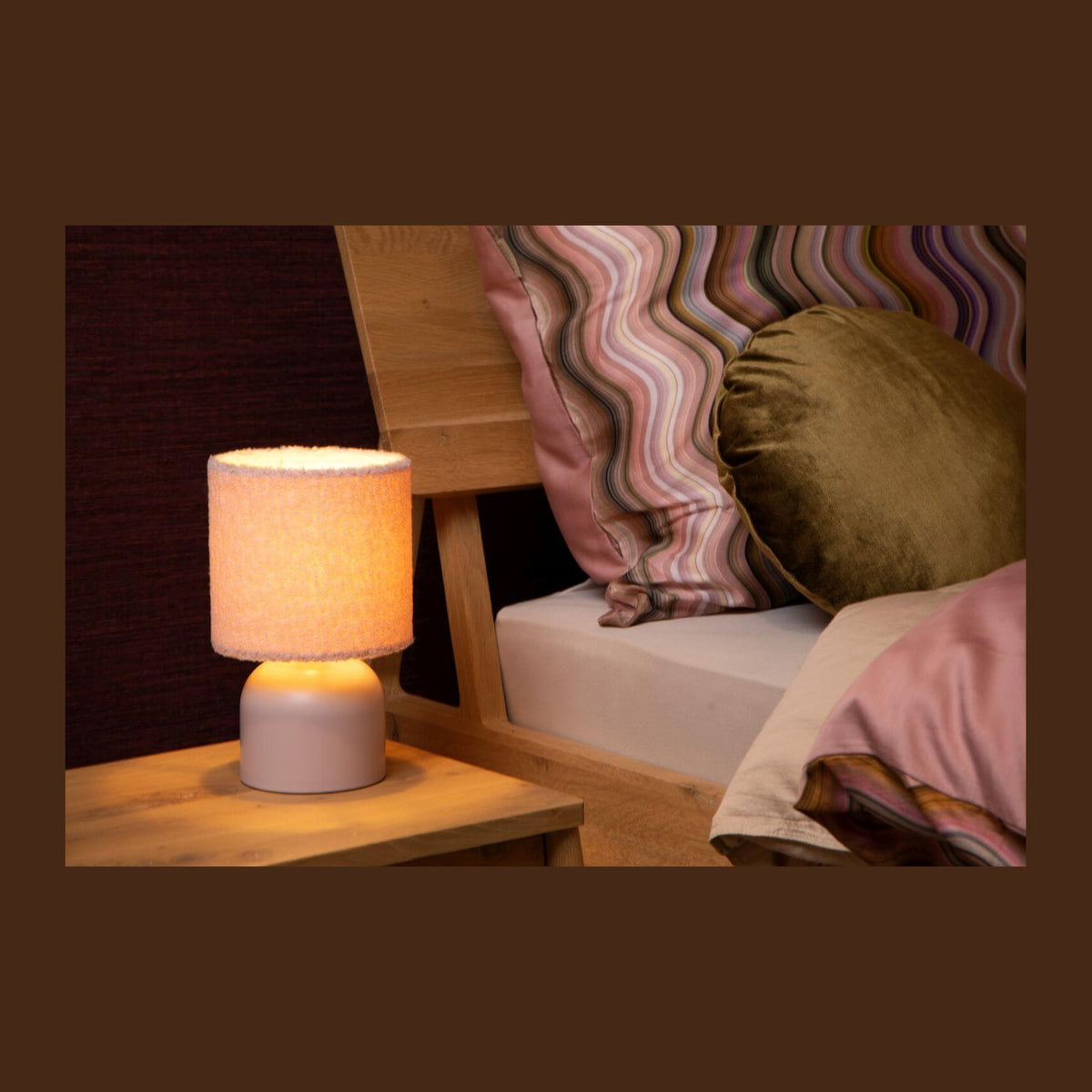Lampe à poser allumée sur une table de chevet en bois, dans une chambre