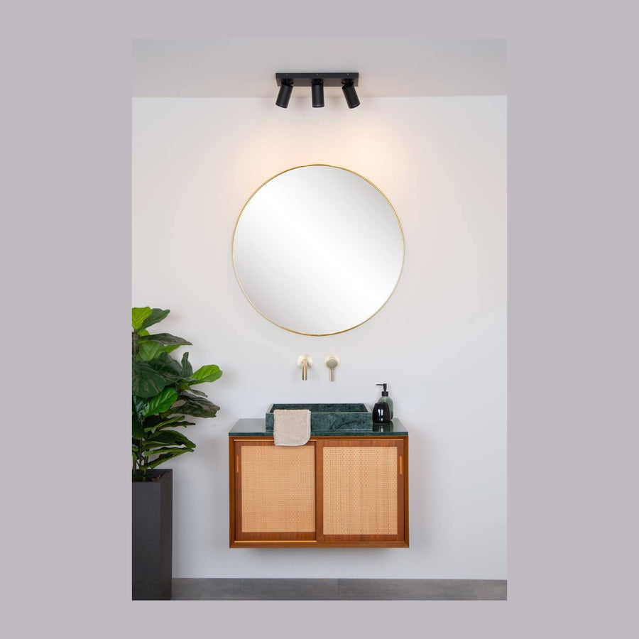 Plafonnier noir trois spots orientables au-dessus d'un miroir rond, salle de bain claire