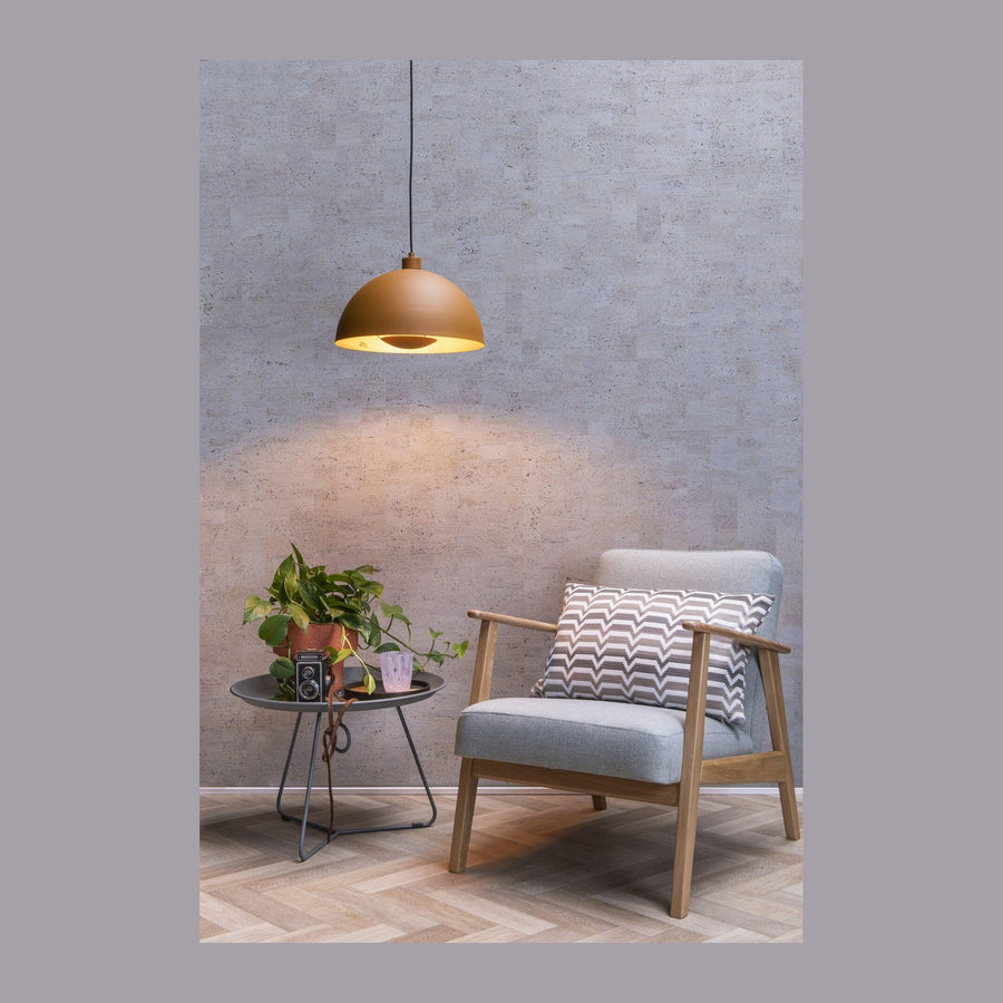 Suspension dorée éclairant un fauteuil gris et une table ronde avec plante verte.