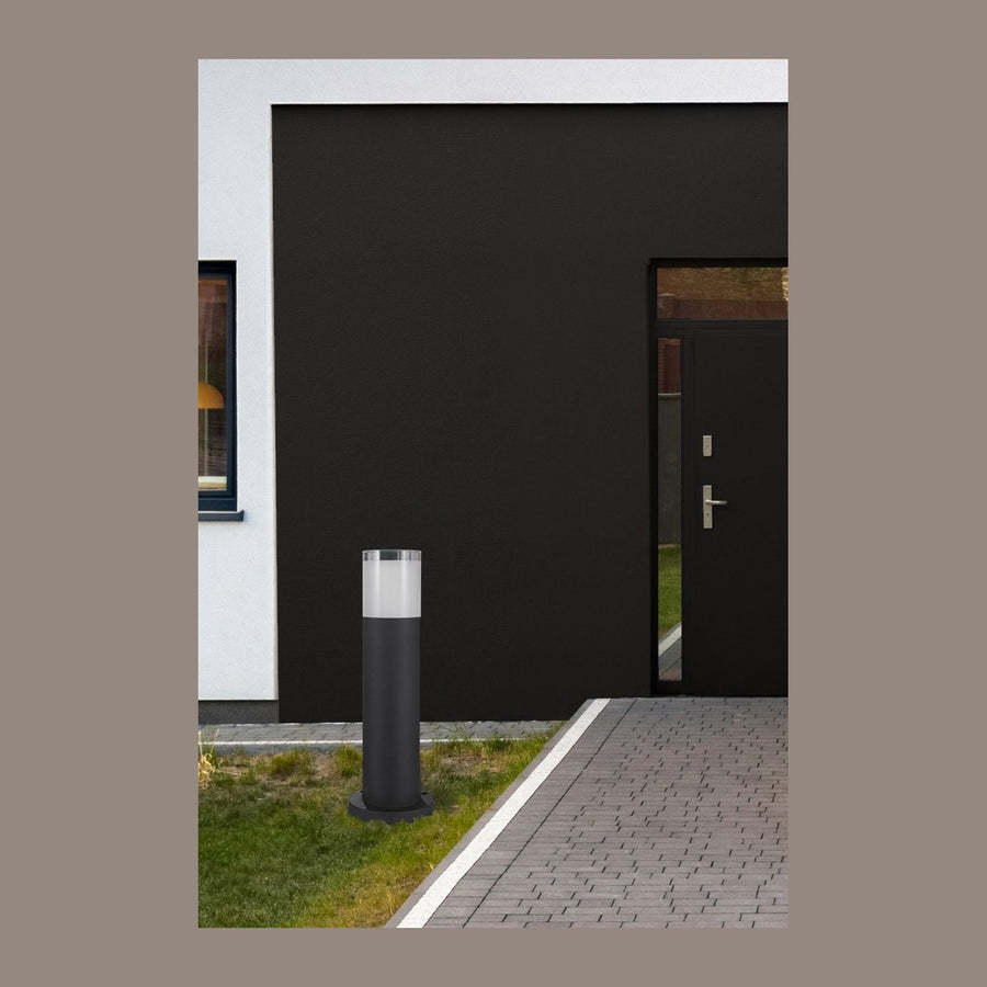 Borne noire installée dans une pelouse devant une façade sombre et une allée pavée.